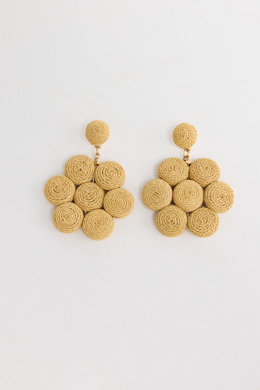 Pair of large statement drop earrings made of seven coiled natural raffia rosettes arranged in a flower shape, with a matching round raffia stud, laid flat on a white background