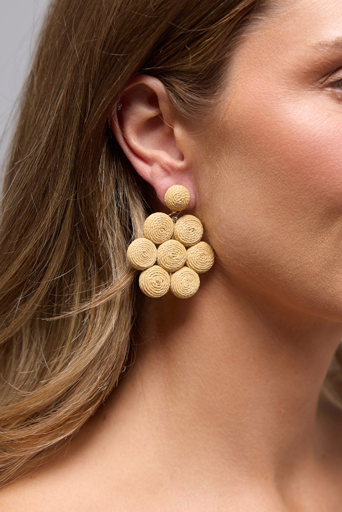 Heritage Earrings in natural worn on the ear, showing the woven raffia rosette texture up close