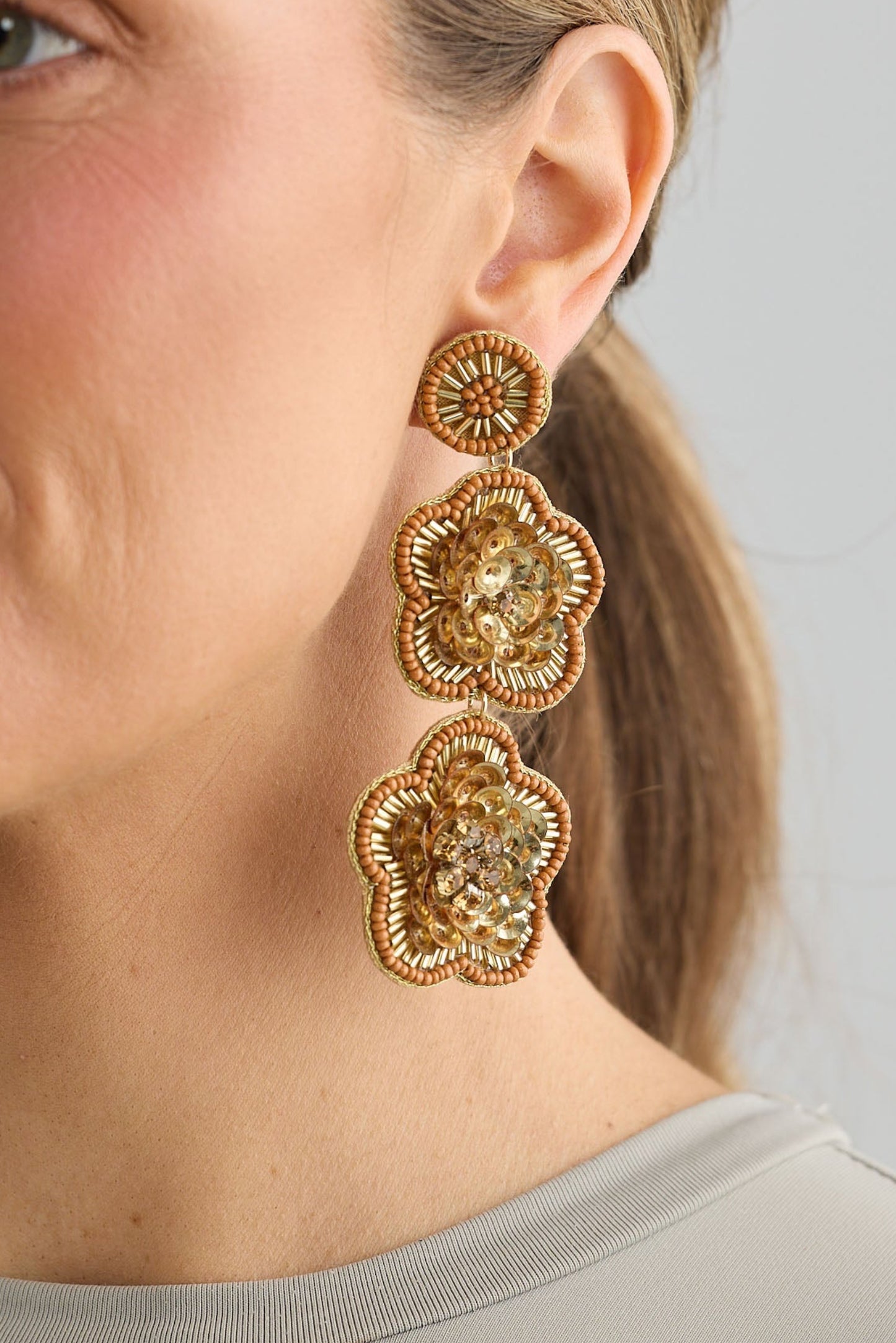 Woman wearing gold floral earrings against a neutral background