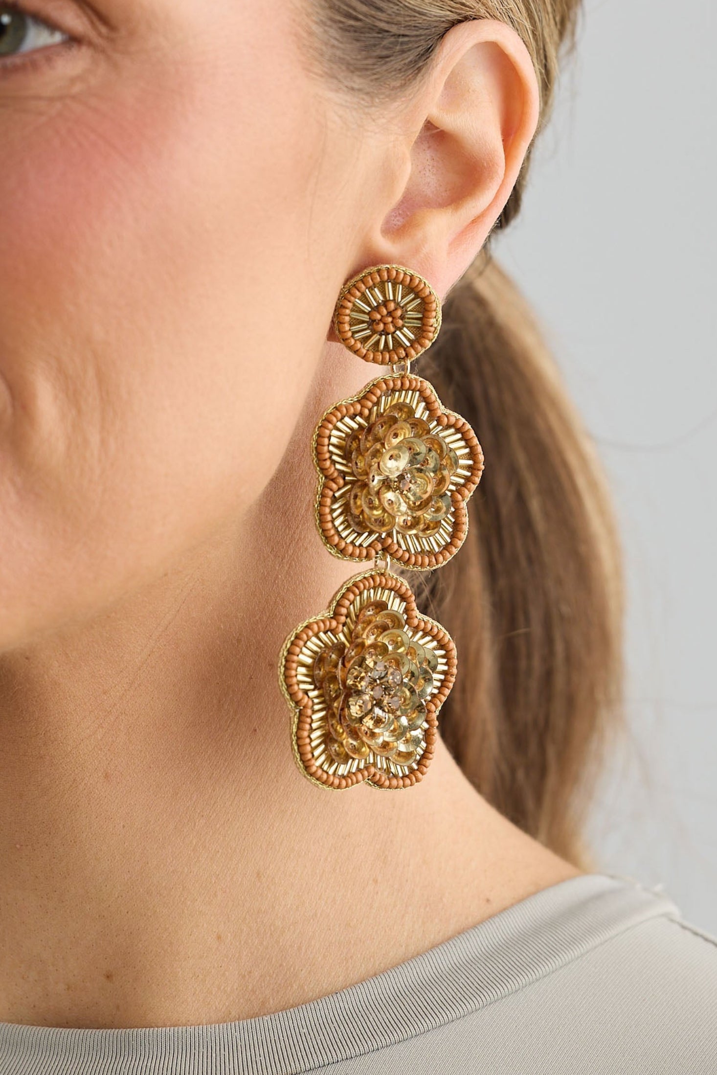 Woman wearing gold floral earrings against a neutral background