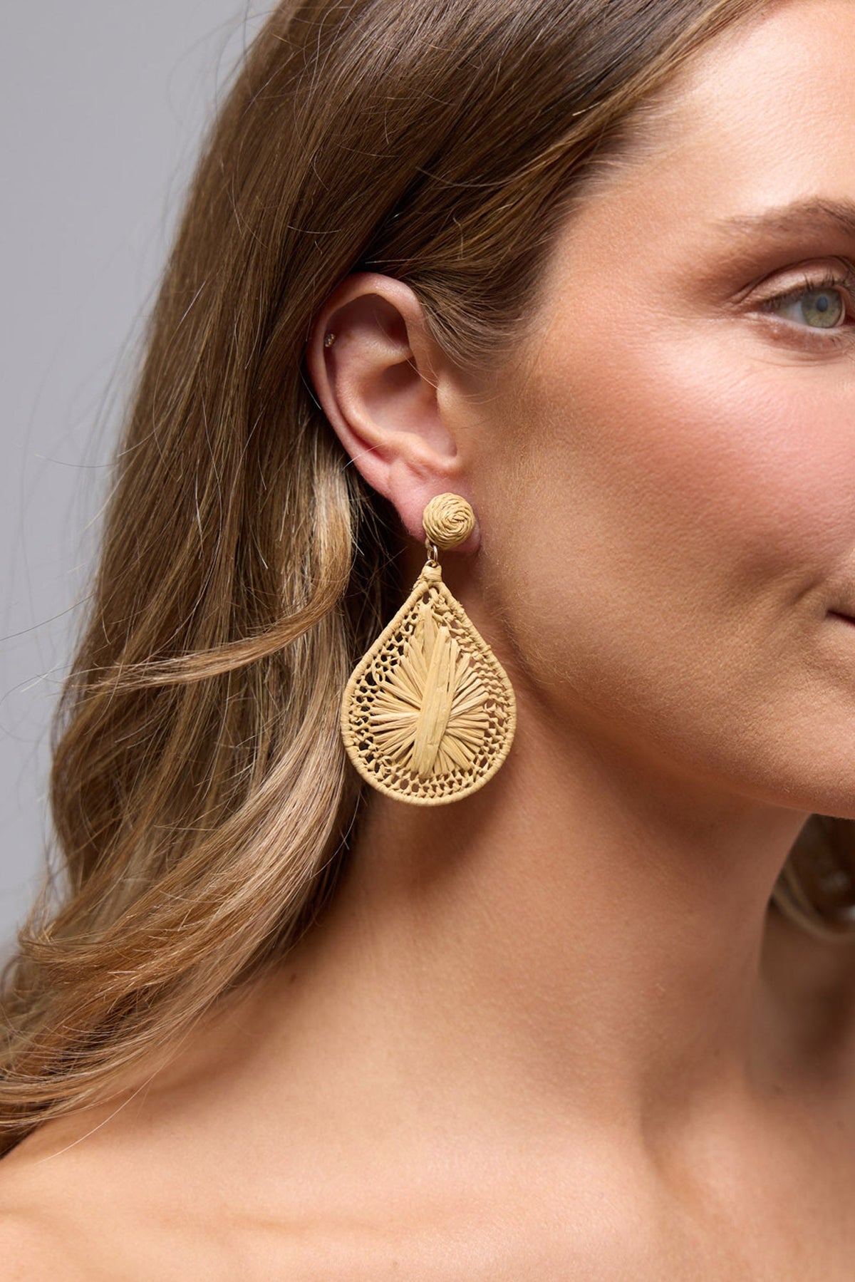 Refined Earrings in natural worn on the ear, showing the woven raffia teardrop shape and texture up close