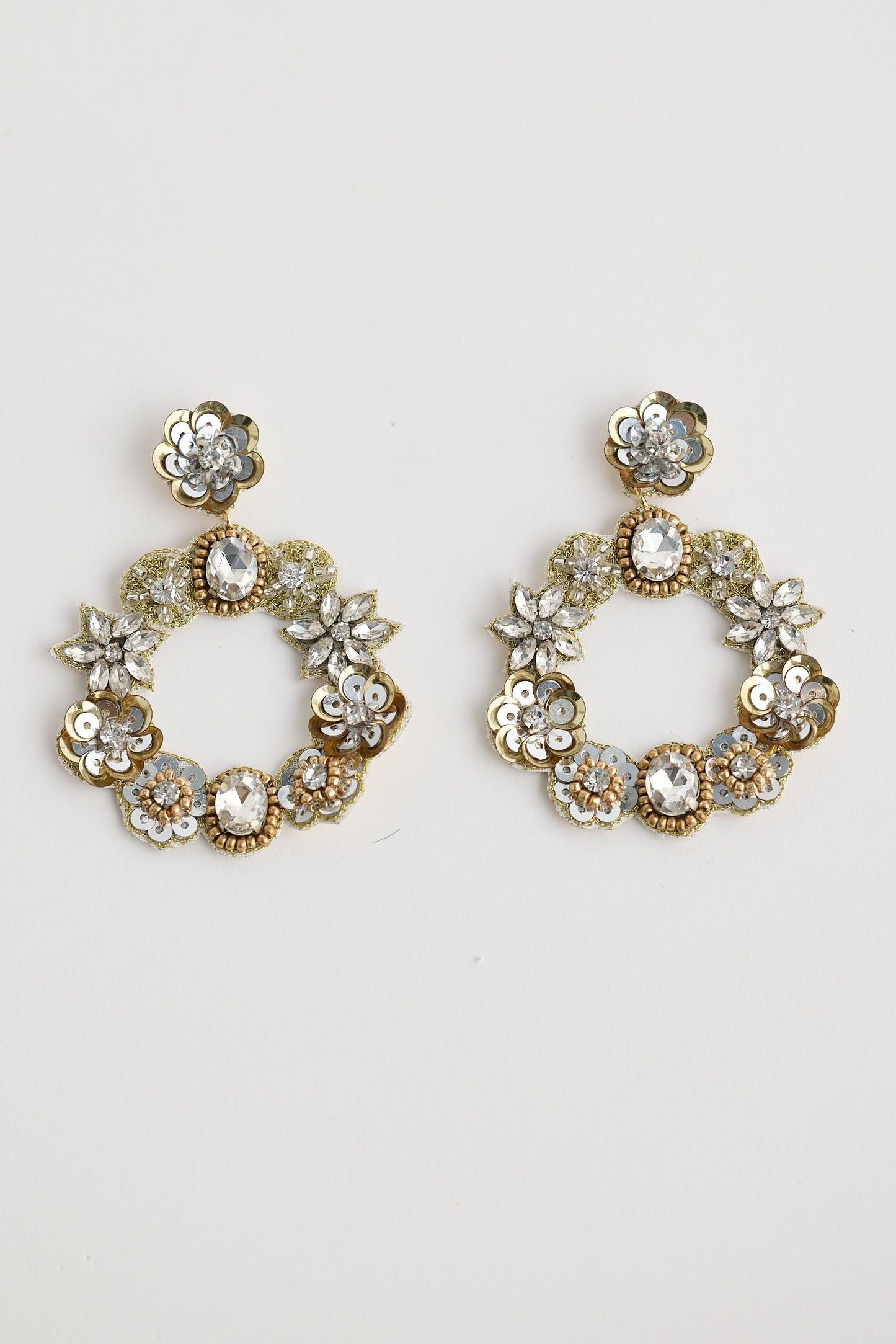 Pair of gold hoop earrings with floral and gemstone details on a light gray background