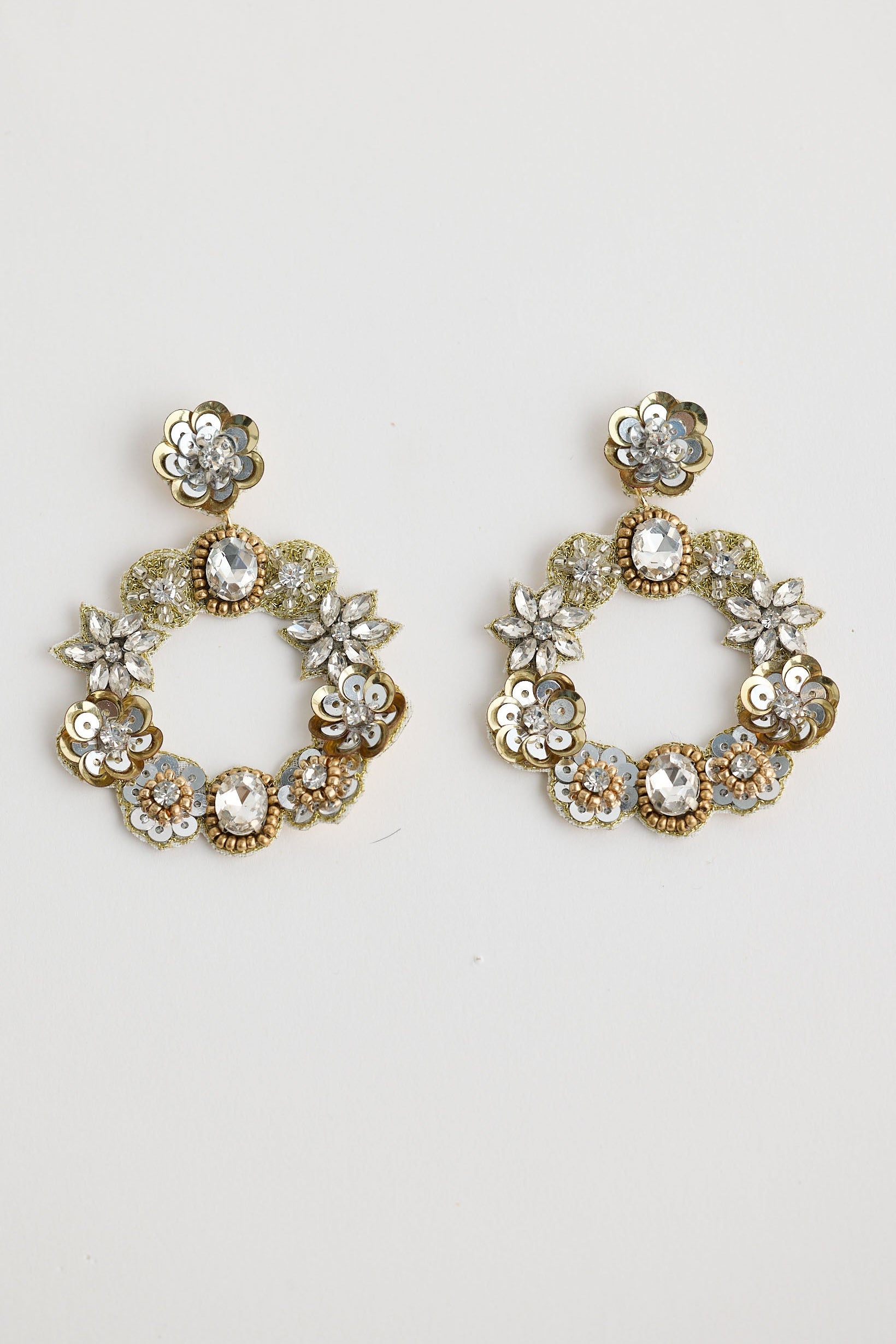 Pair of gold hoop earrings with floral and gemstone details on a light gray background