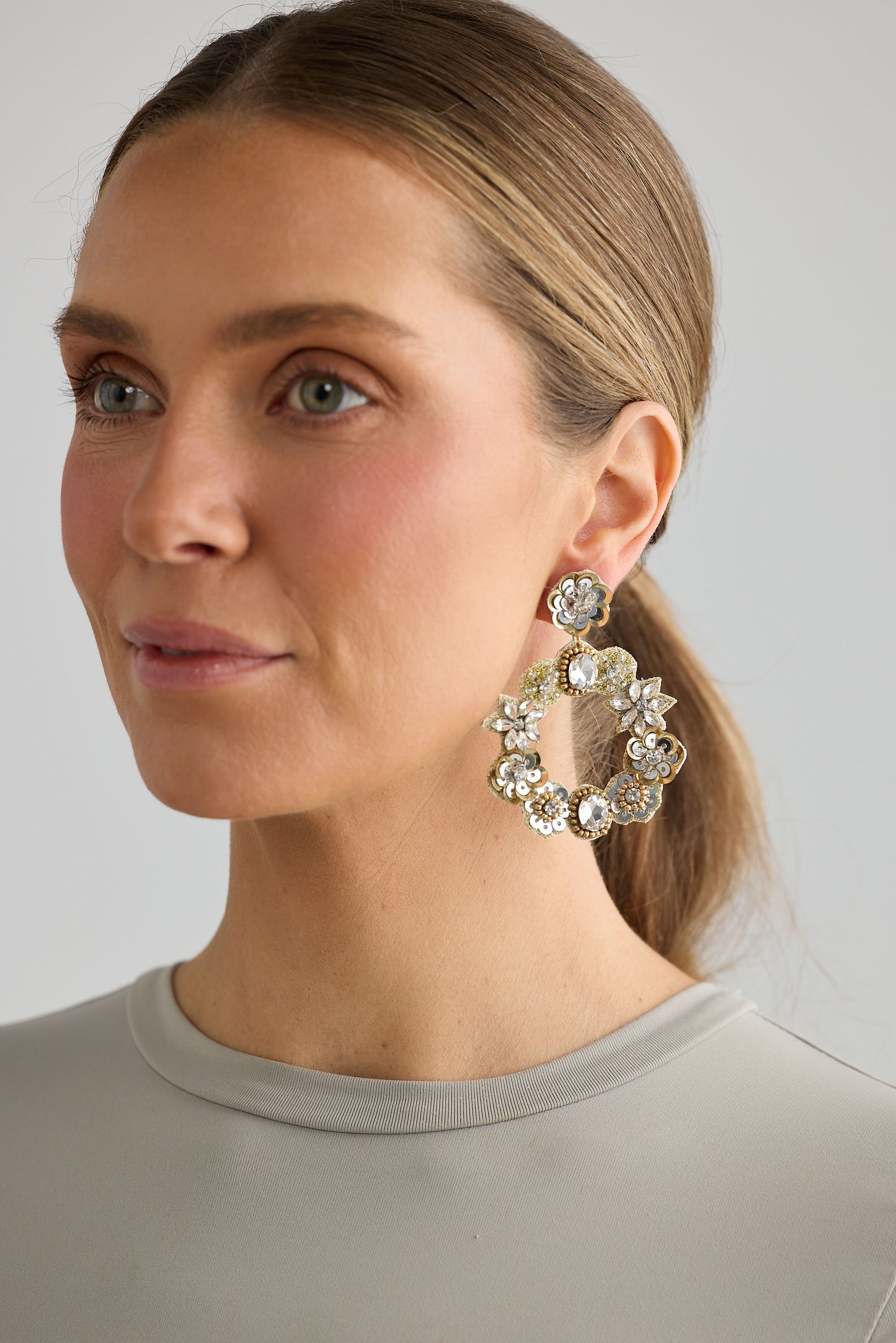 Woman wearing large, ornate earrings against a neutral background