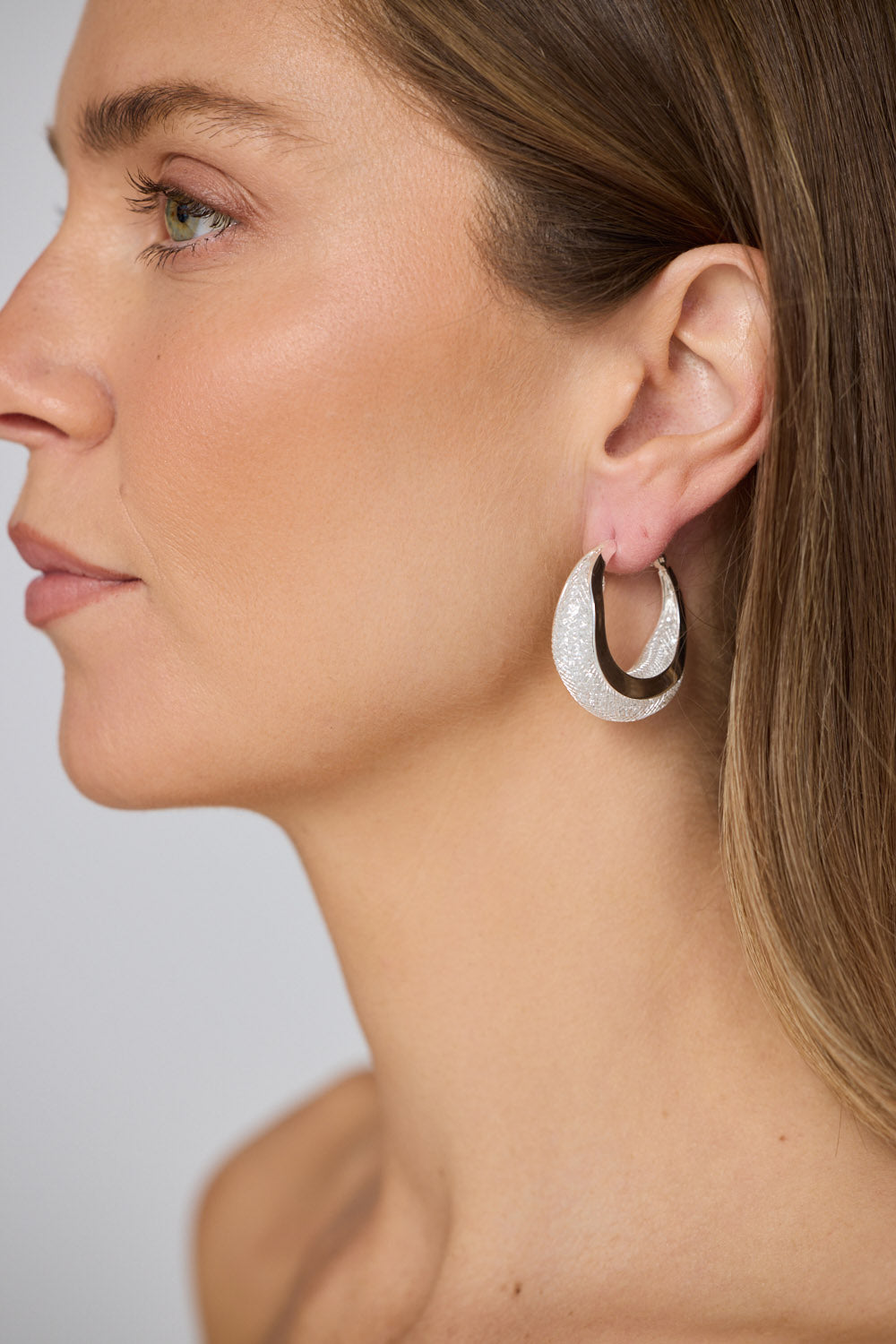 Model wearing Eclipse Earrings in silver with soft textured finish, side profile view on neutral background