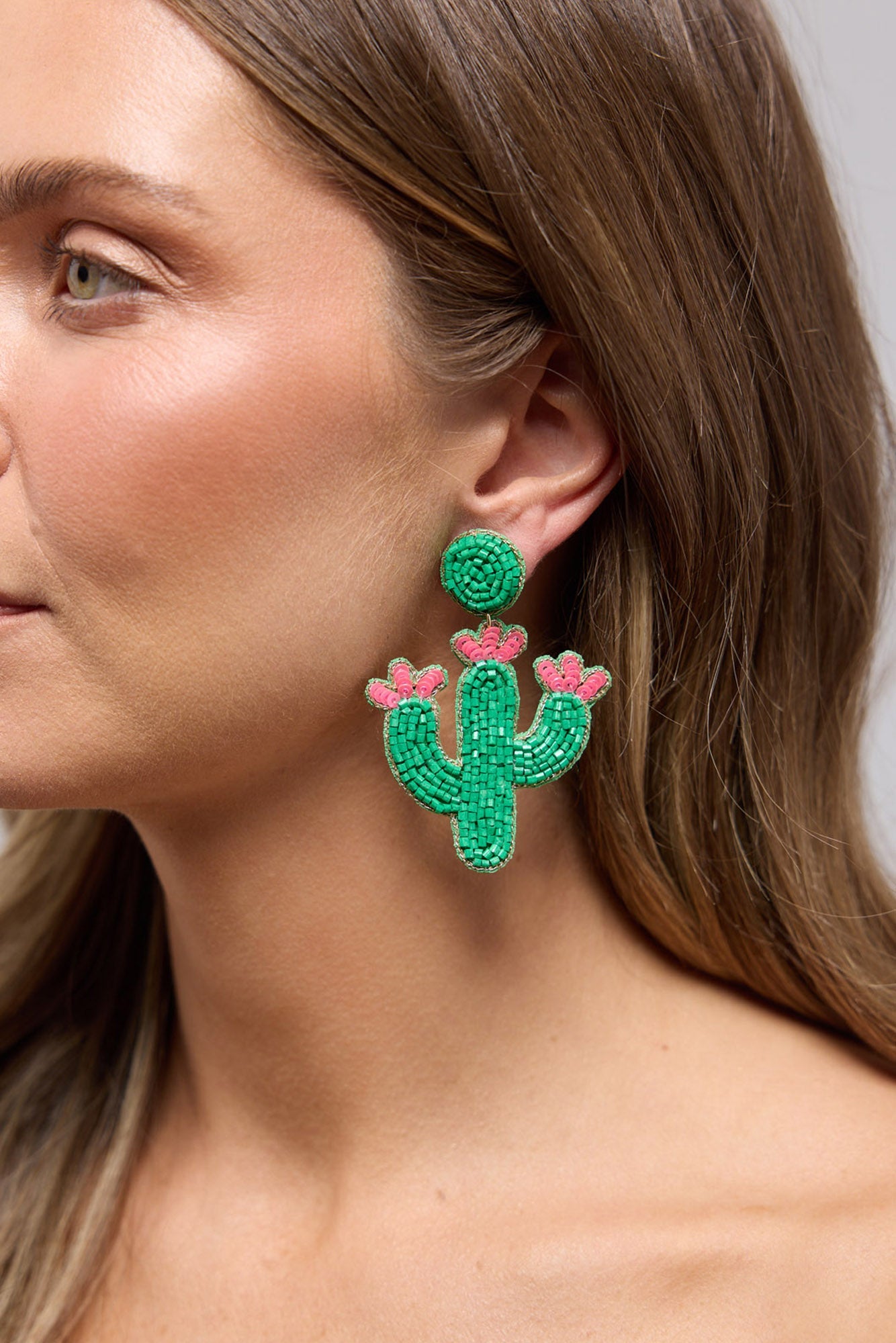 Cacti Earrings in green worn on the ear, showing the beaded cactus shape and pink flower detail up close
