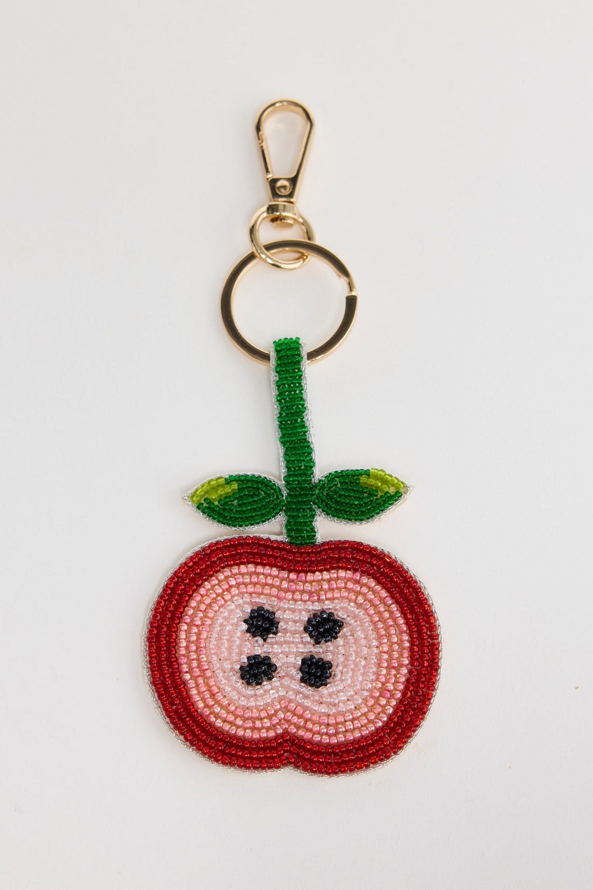 Beaded keyring in the shape of a sliced apple cross-section, with a red outer border, pink and cream inner layers and black seed detail, with a green beaded stem and leaves, attached to a gold-tone clasp and split ring, shown on a white background