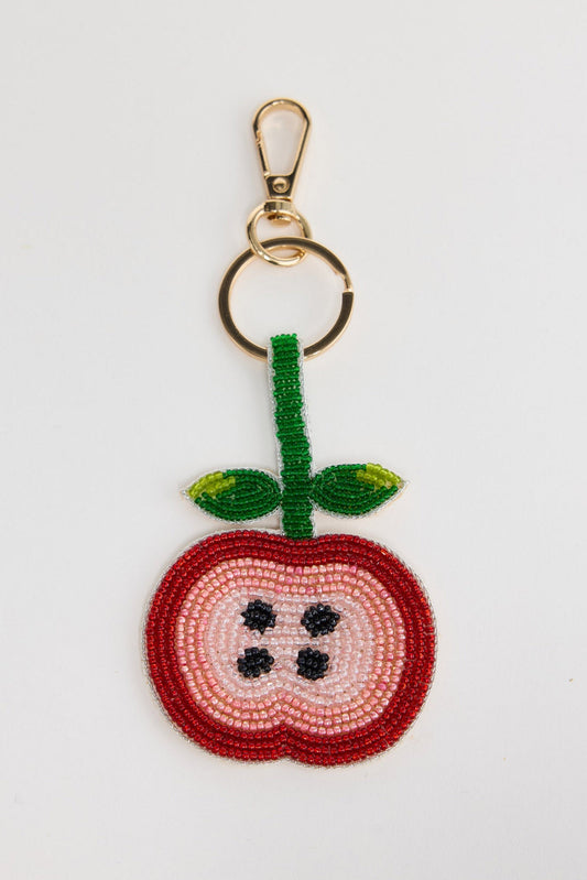 Beaded keyring in the shape of a sliced apple cross-section, with a red outer border, pink and cream inner layers and black seed detail, with a green beaded stem and leaves, attached to a gold-tone clasp and split ring, shown on a white background