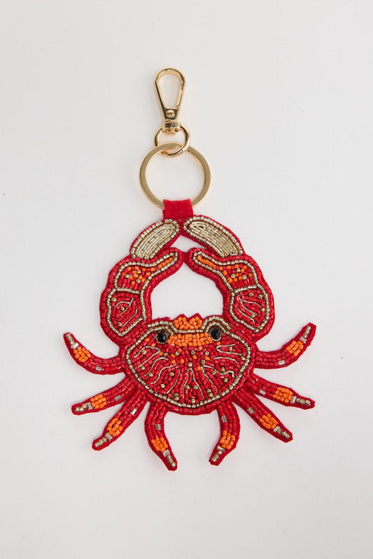 Large beaded crab keyring in bold red seed beads with orange accent claws, gold-tone bugle bead legs and black bead eyes, attached to a gold-tone clasp and split ring via a red leather tab, shown on a white background