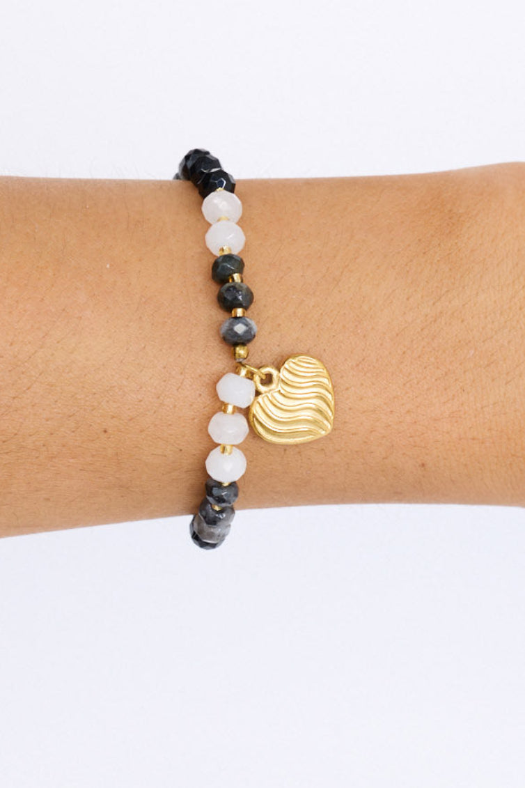 Model wearing Huda Bracelet in black with statement gold charm detail, angled on-wrist view on neutral background