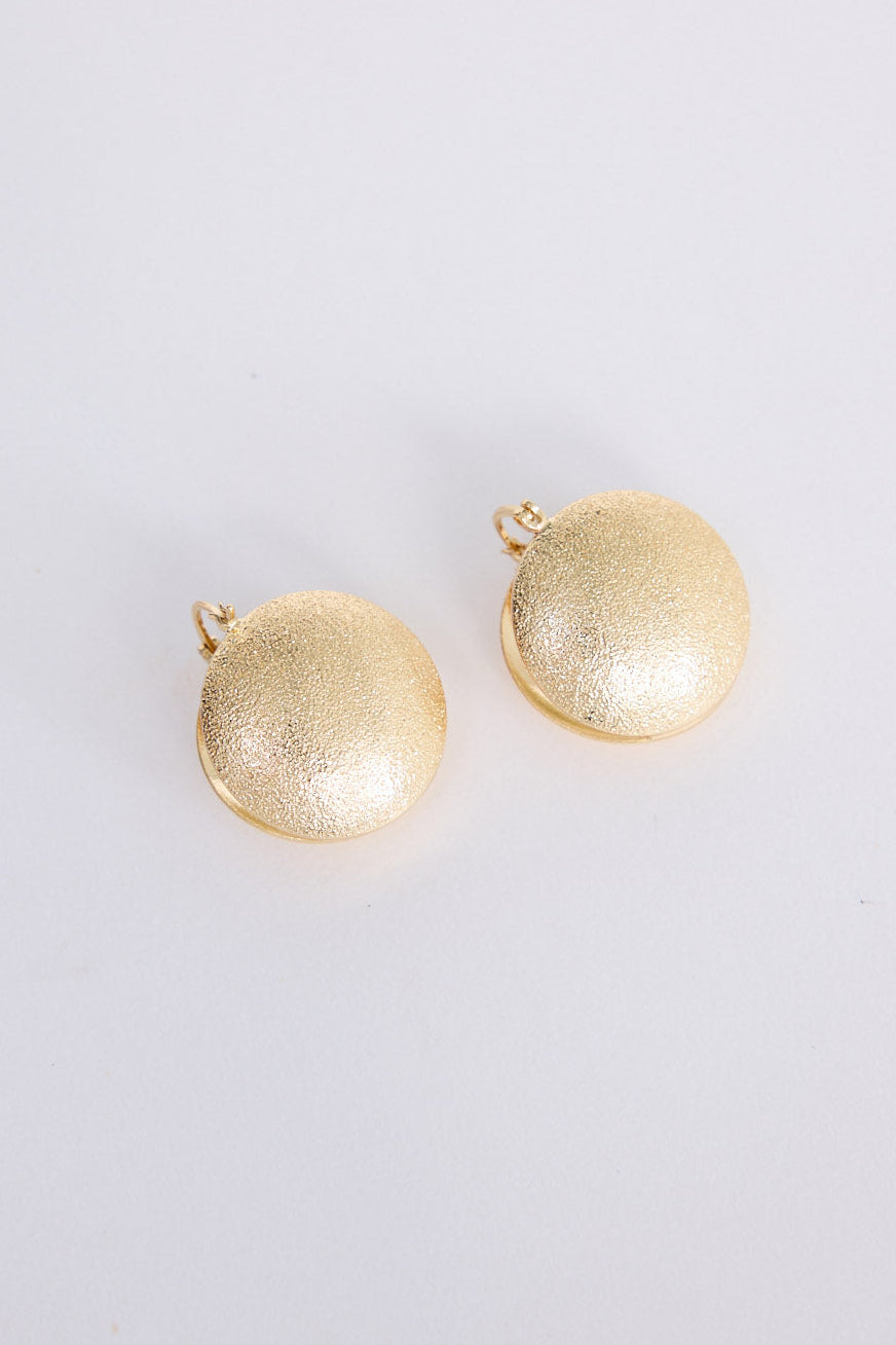 Model wearing Sue Earrings in gold with a brushed textured finish, side profile view on neutral background