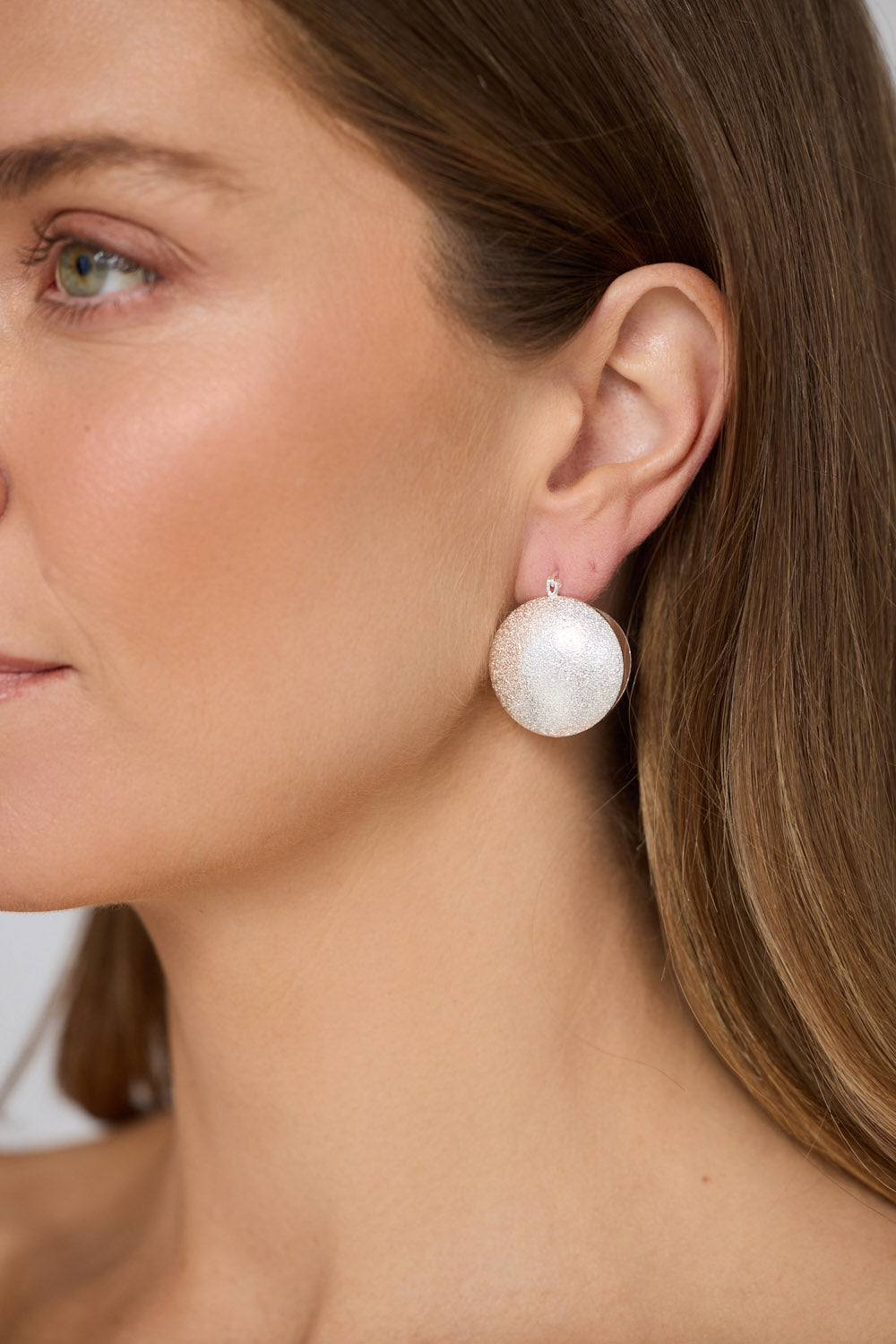 Model wearing Sue Earrings in silver with a brushed textured finish, side profile view on neutral background