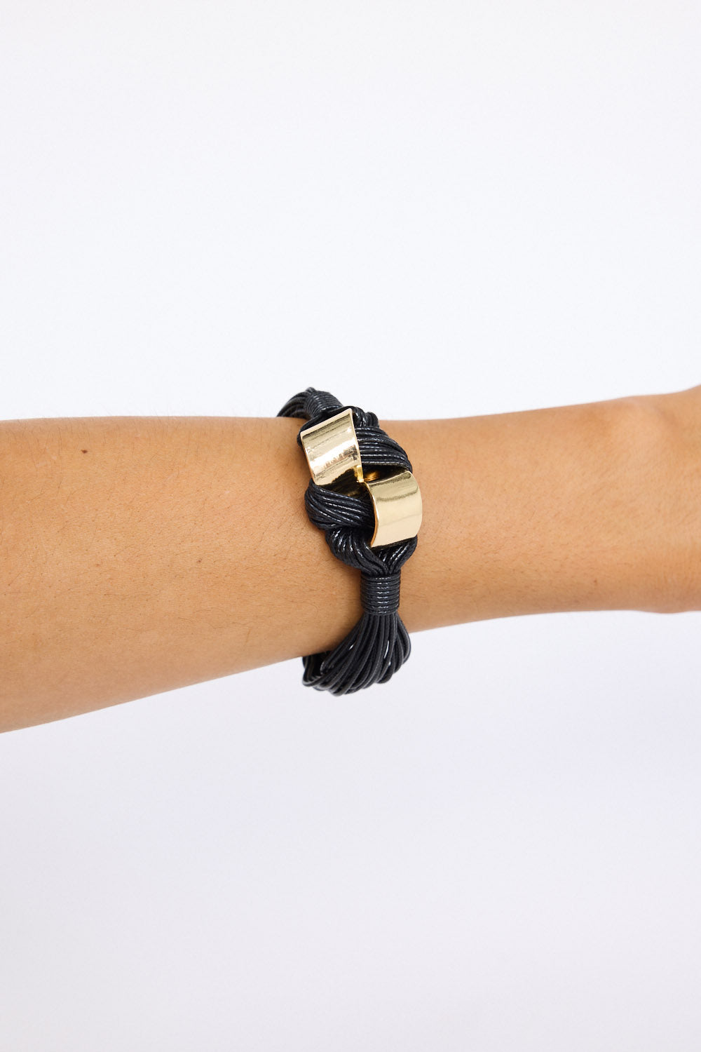 Model wearing Kazima Bracelet in black with bold knot detailing and metal accents, on-wrist view on neutral background