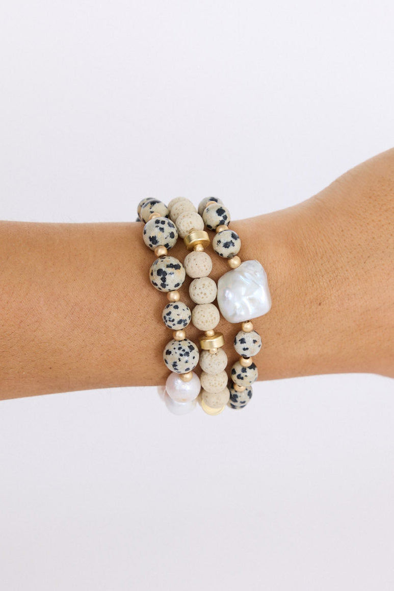 Model wearing Kendra Stack Bracelet in grey with natural stones and mother of pearl feature bead, on-wrist view on neutral background