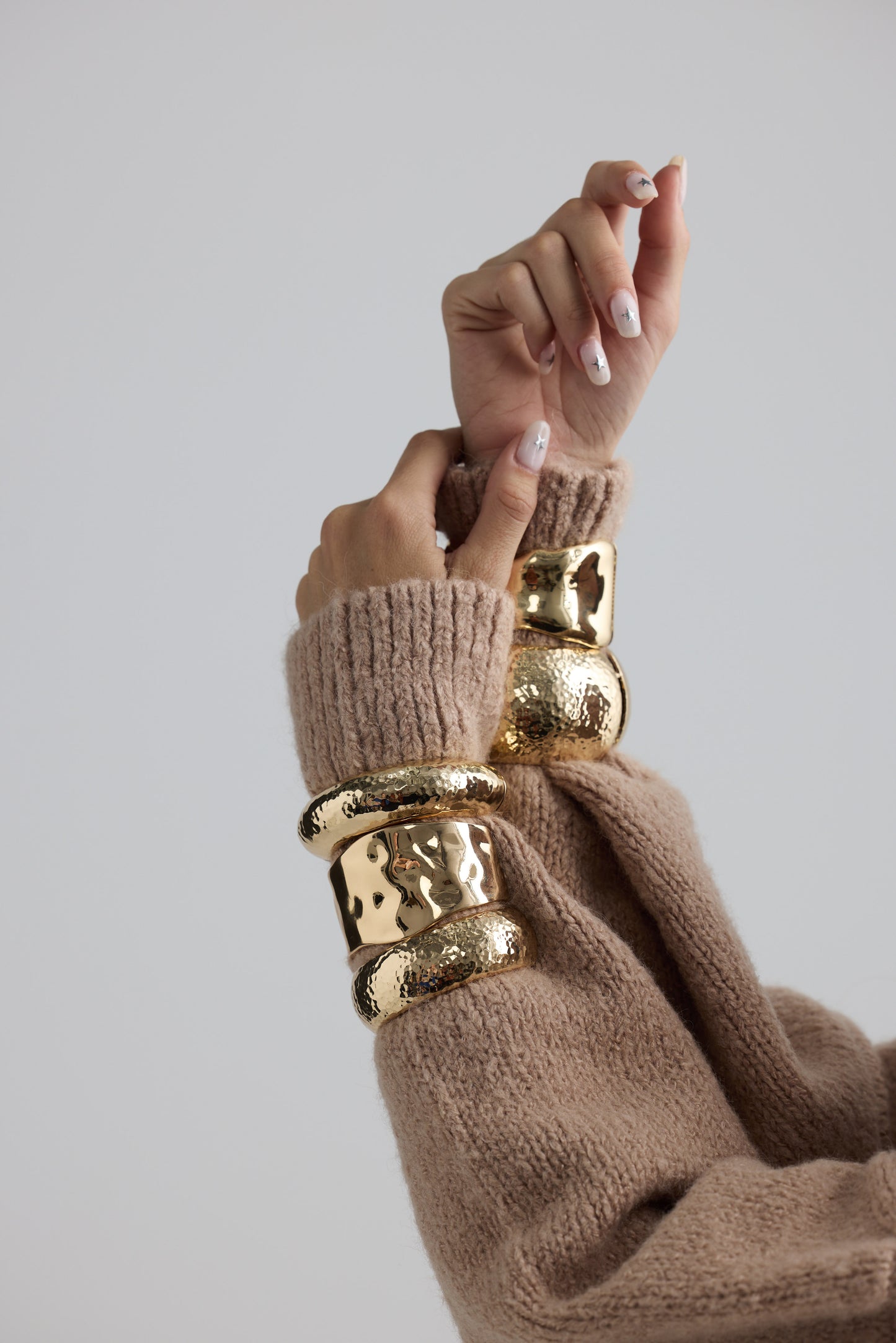 Model wearing Maura Bangle in gold with snap lock closure and hinge for easy wear, on-wrist view on neutral background