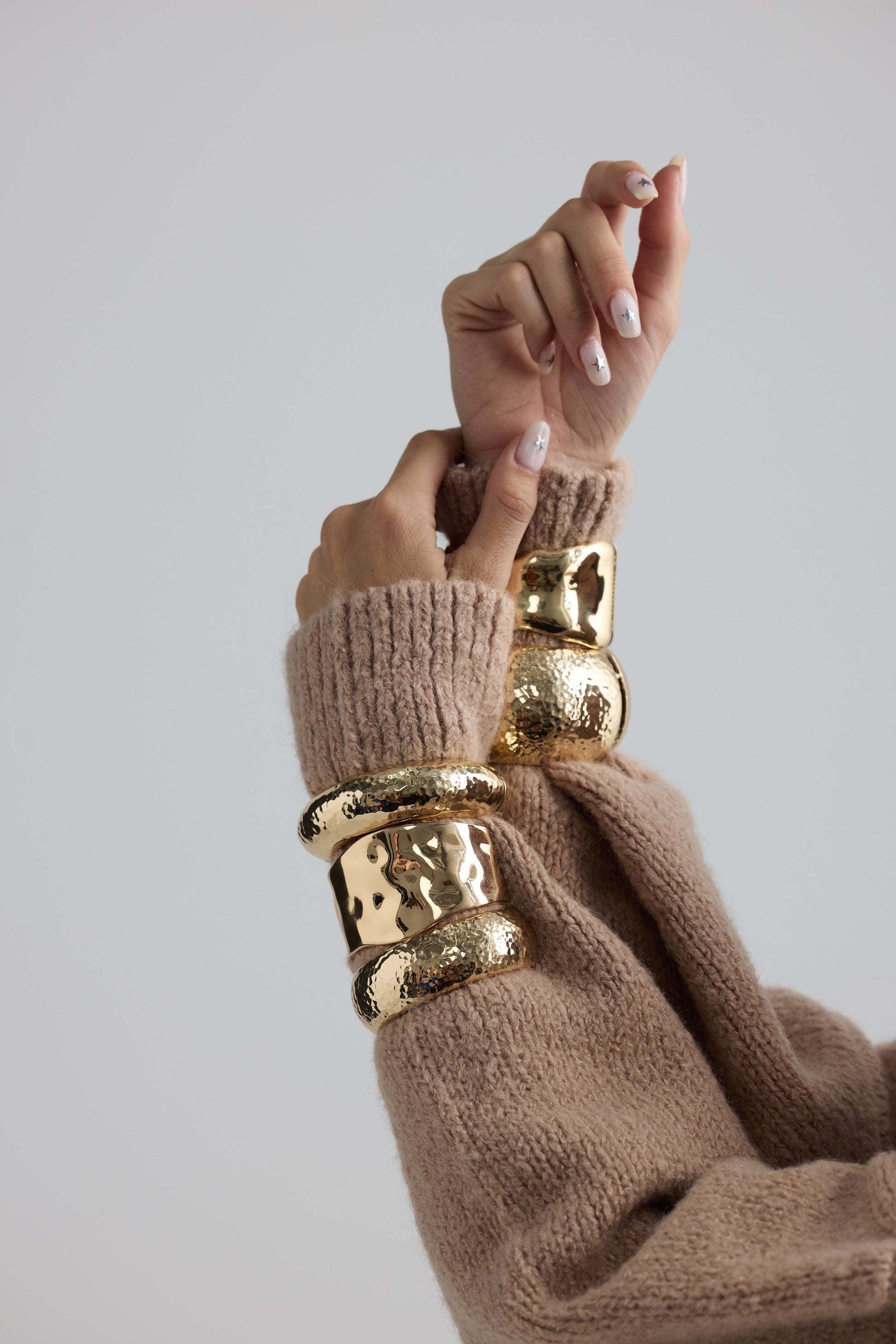 Model wearing Maura Bangle in gold with snap lock closure and hinge for easy wear, on-wrist view on neutral background