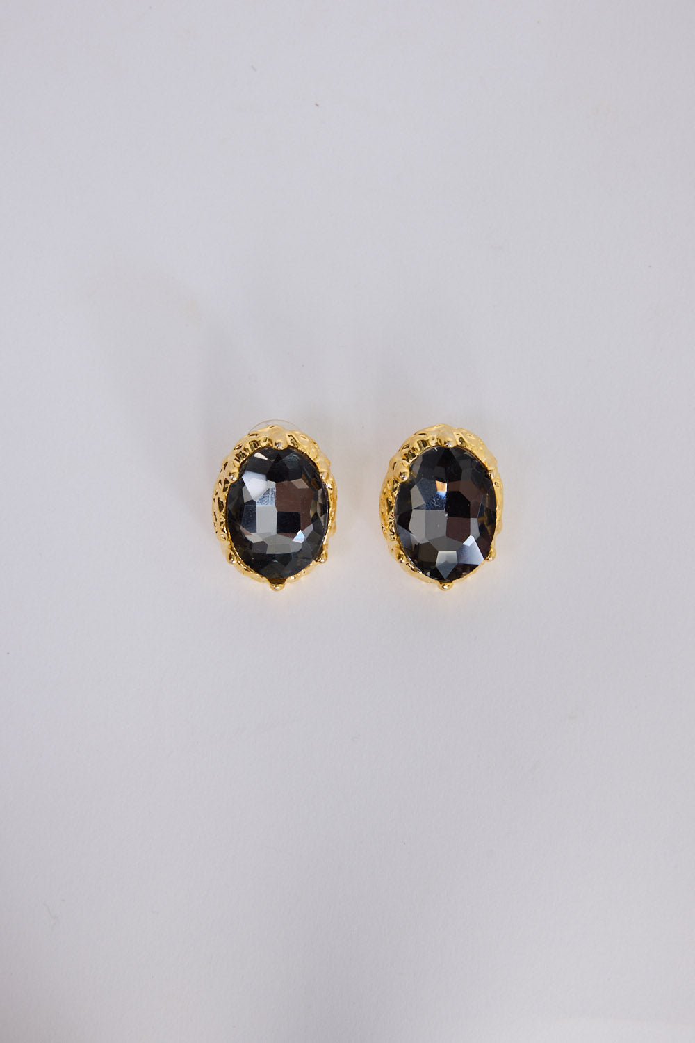 Unice Earrings in smoke with a faceted stone set in a textured gold surround, angled view on white background