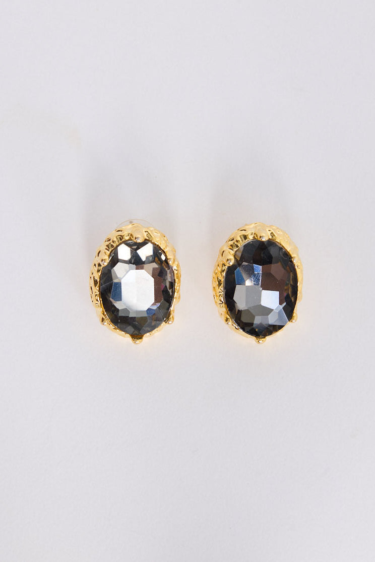 Model wearing Unice Earrings in smoke with a faceted stone set in a textured gold surround, ear detail view on neutral background