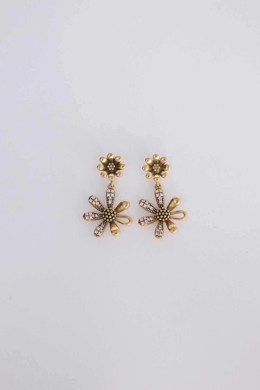 A pair of gold-toned flower-shaped drop earrings with textured centers and small clear rhinestone accents, displayed on a plain light gray background.