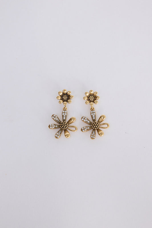 A pair of gold-toned flower-shaped drop earrings with textured centers and small clear rhinestone accents, displayed on a plain light gray background.