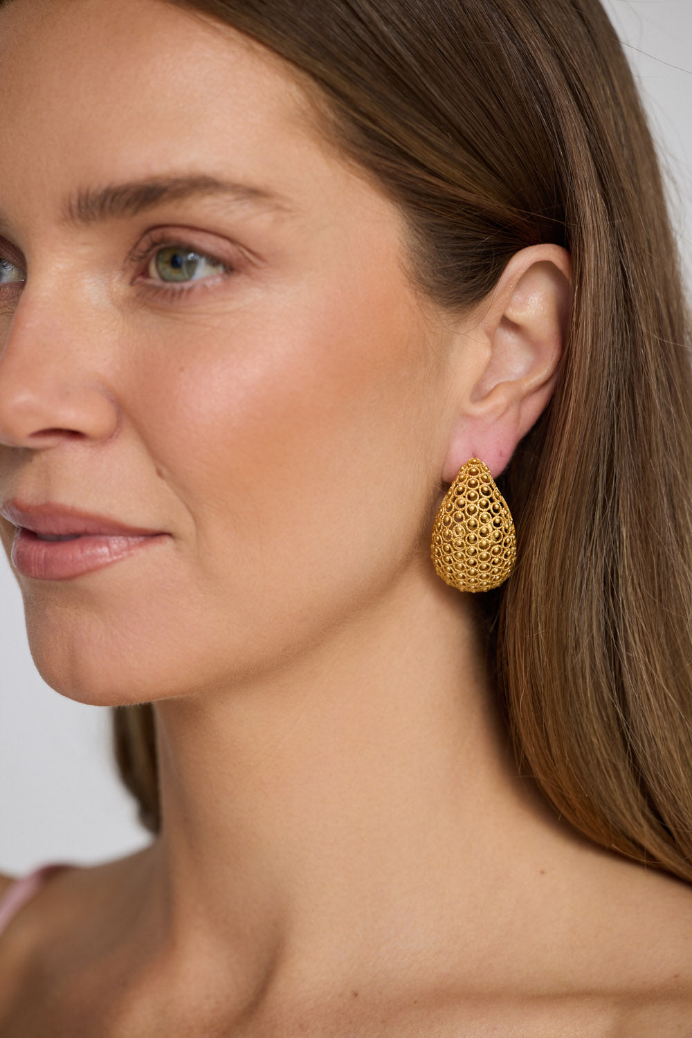 Model wearing Meadow Earrings in gold with woven texture detailing, styled ear close-up on neutral background