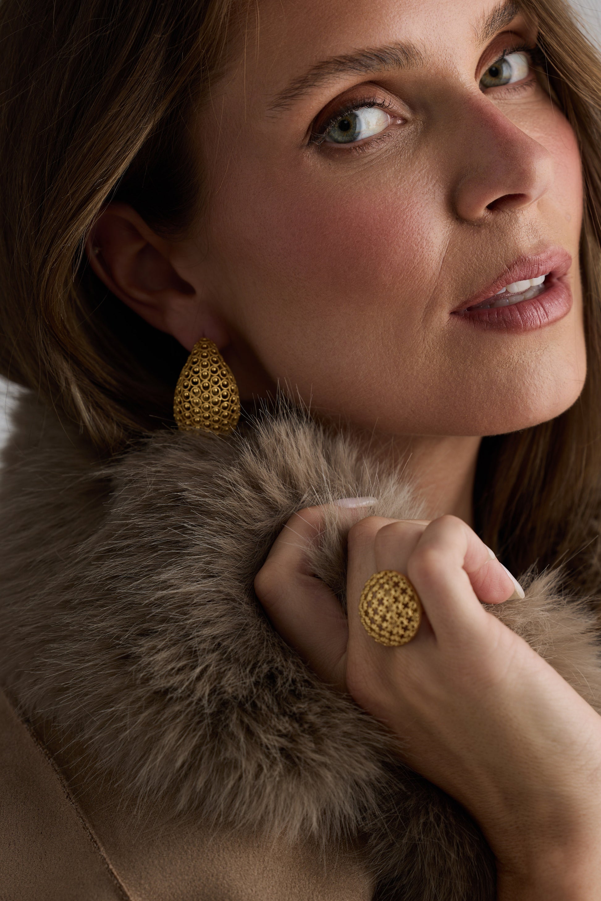 Model wearing Meadow Earrings in gold with woven texture detailing, side angle view on neutral background