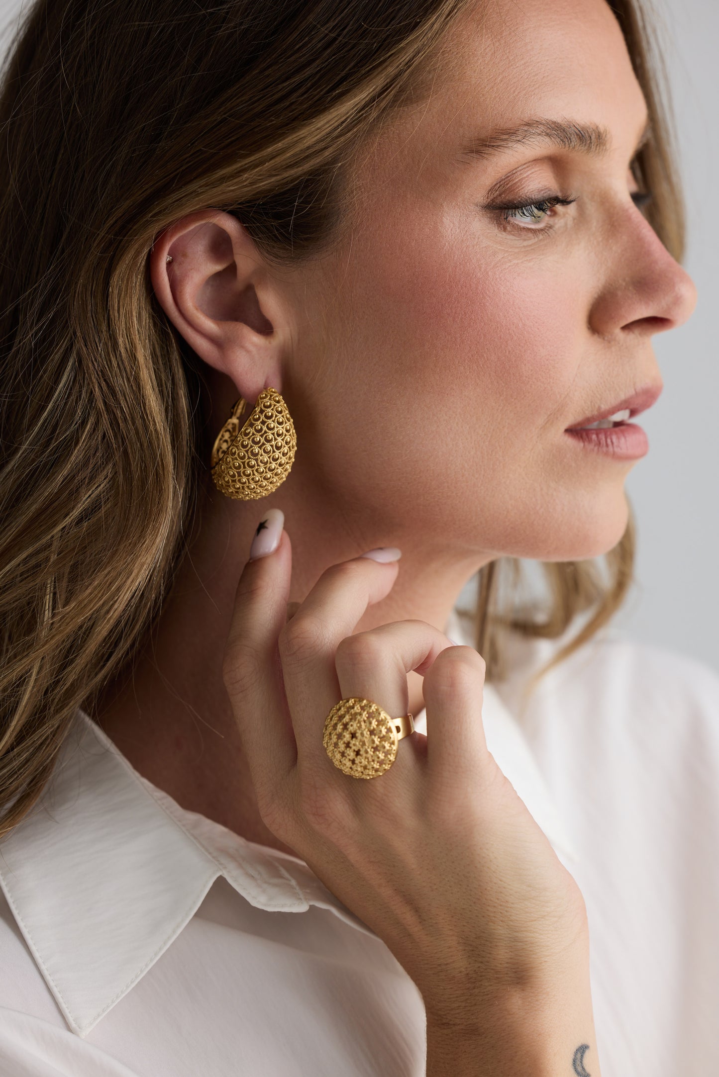 Model wearing Meadow Earrings in gold with woven texture detailing, alternate model view on neutral background