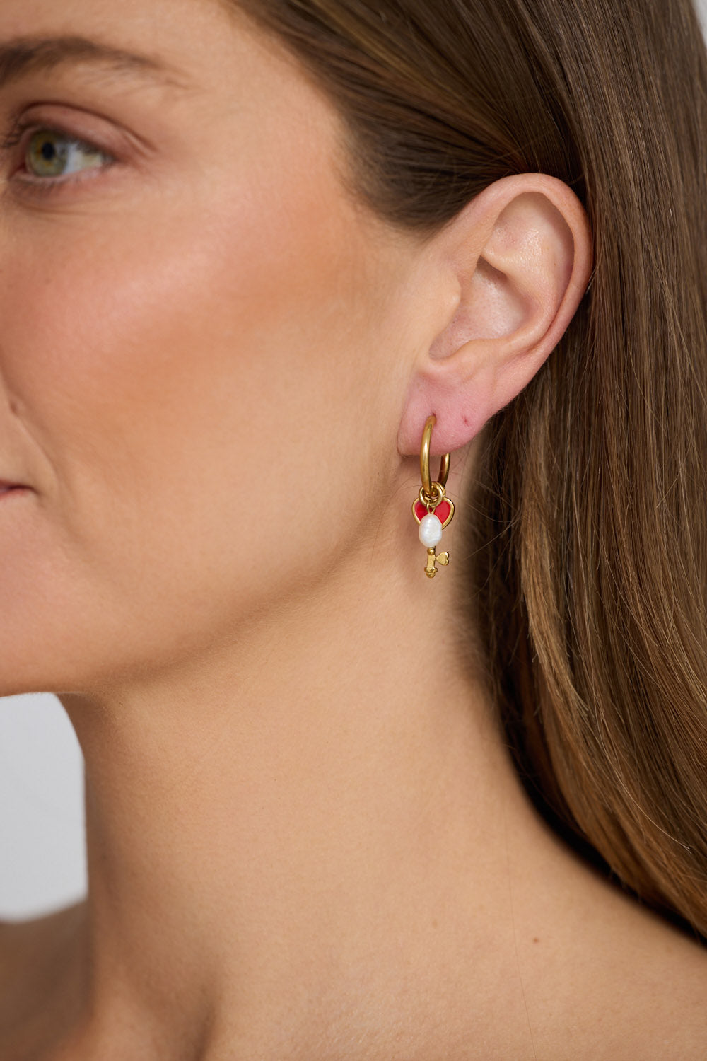 Model wearing Lockheart Earrings in gold with heart and key charm detailing, model close-up view on neutral background
