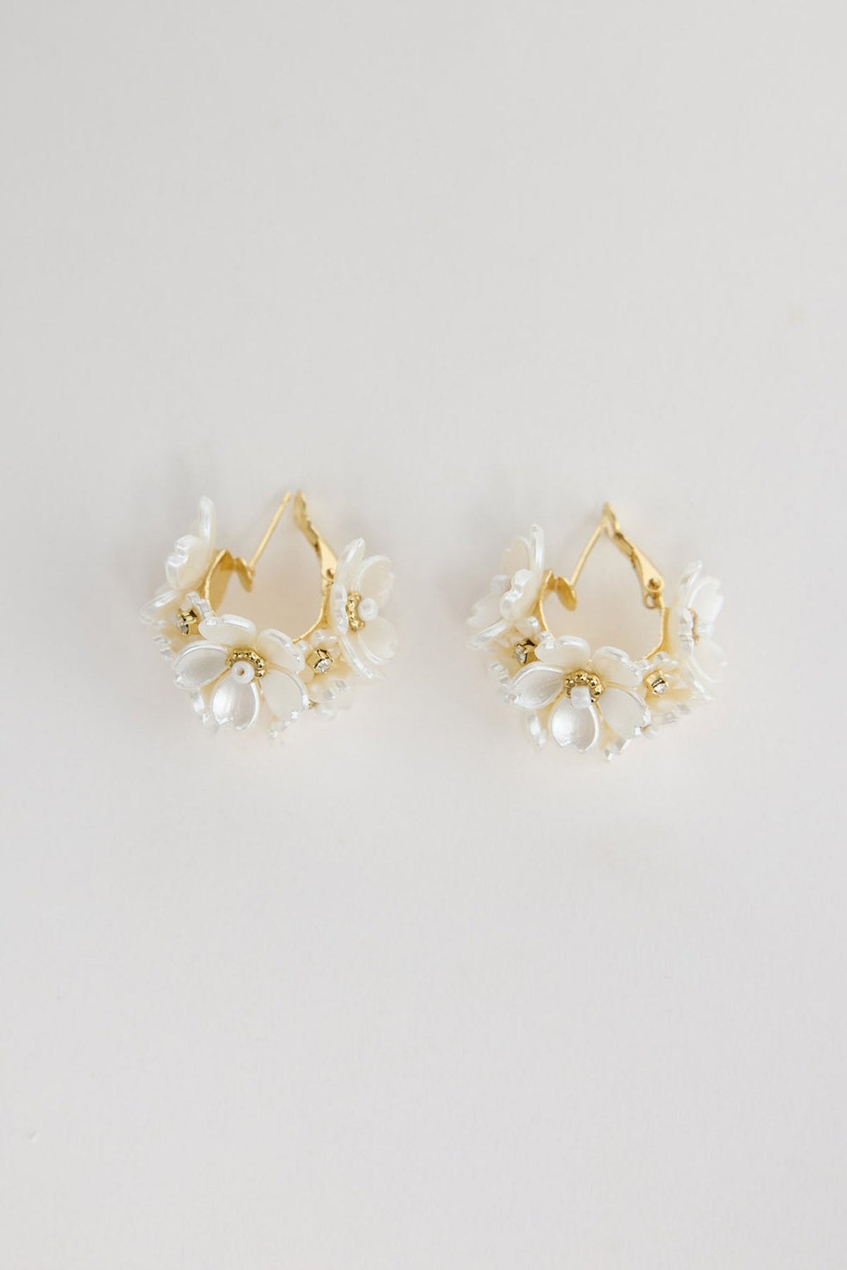 Pair of gold-tone hoop earrings with clusters of white acrylic flower petals and crystal accents, laid flat on a white background