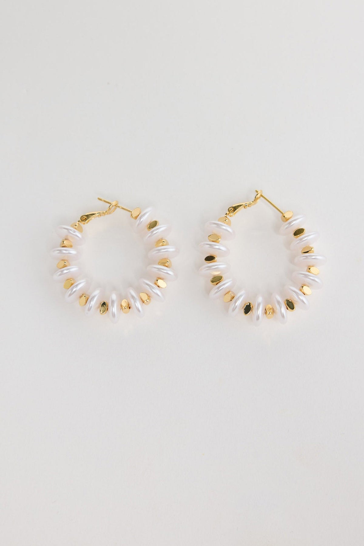Pair of gold-tone hoop earrings made of stacked white pearl-look rondelle beads with small gold accents, laid flat on a white background