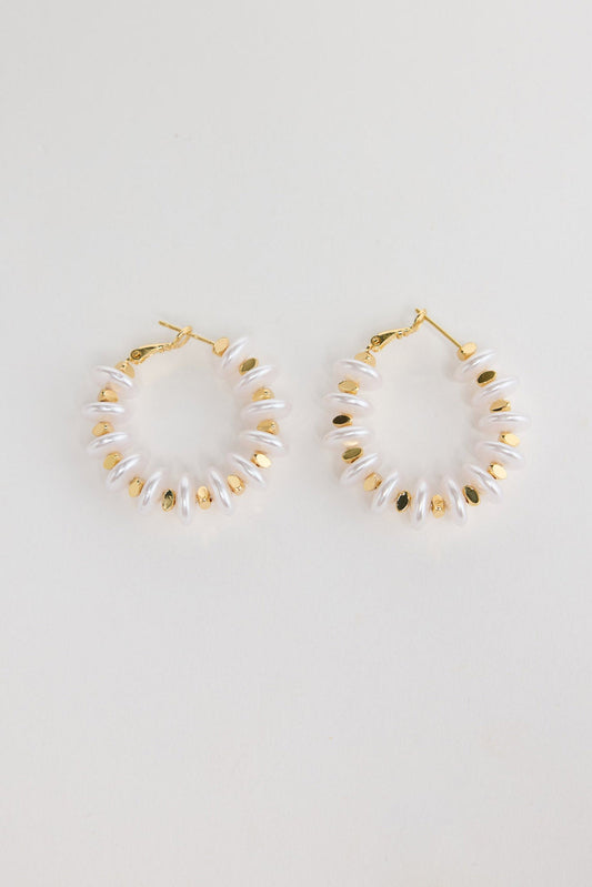 Pair of gold-tone hoop earrings made of stacked white pearl-look rondelle beads with small gold accents, laid flat on a white background