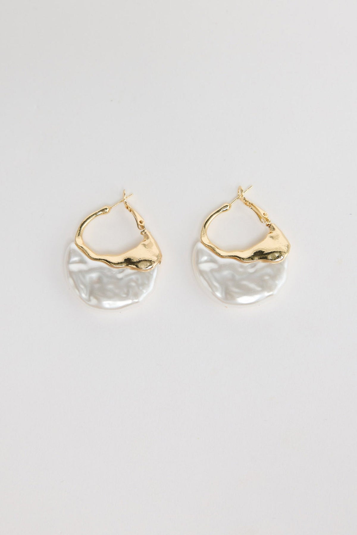 Pair of organic-shaped gold-tone hoop earrings with a textured white pearl-look resin drop, laid flat on a white background