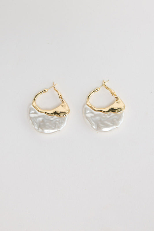 Pair of organic-shaped gold-tone hoop earrings with a textured white pearl-look resin drop, laid flat on a white background