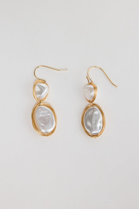 Pair of gold-tone double drop earrings with two white pearl-look stones wrapped in fine wire, laid flat on a white background