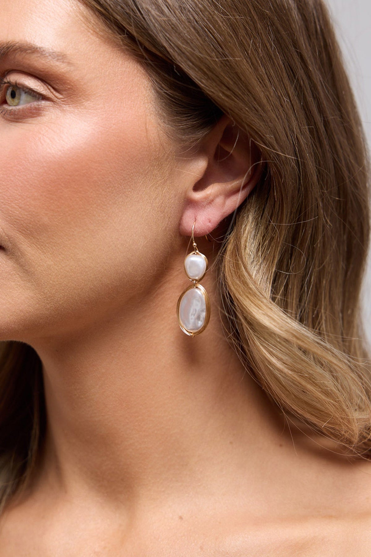 Close-up of a model wearing the gold-tone double drop earring with white pearl-look stones