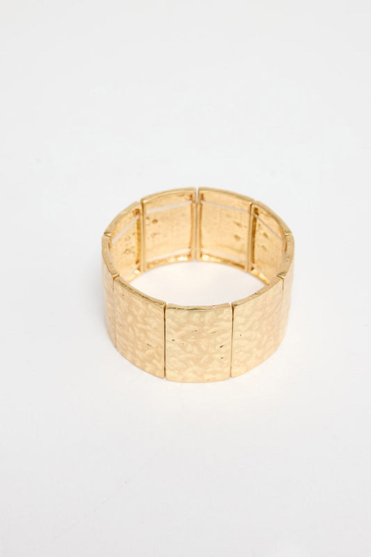 Wide stretch cuff bracelet made of large hammered gold-tone rectangular panels on an elastic band, shown at an angle on a white background