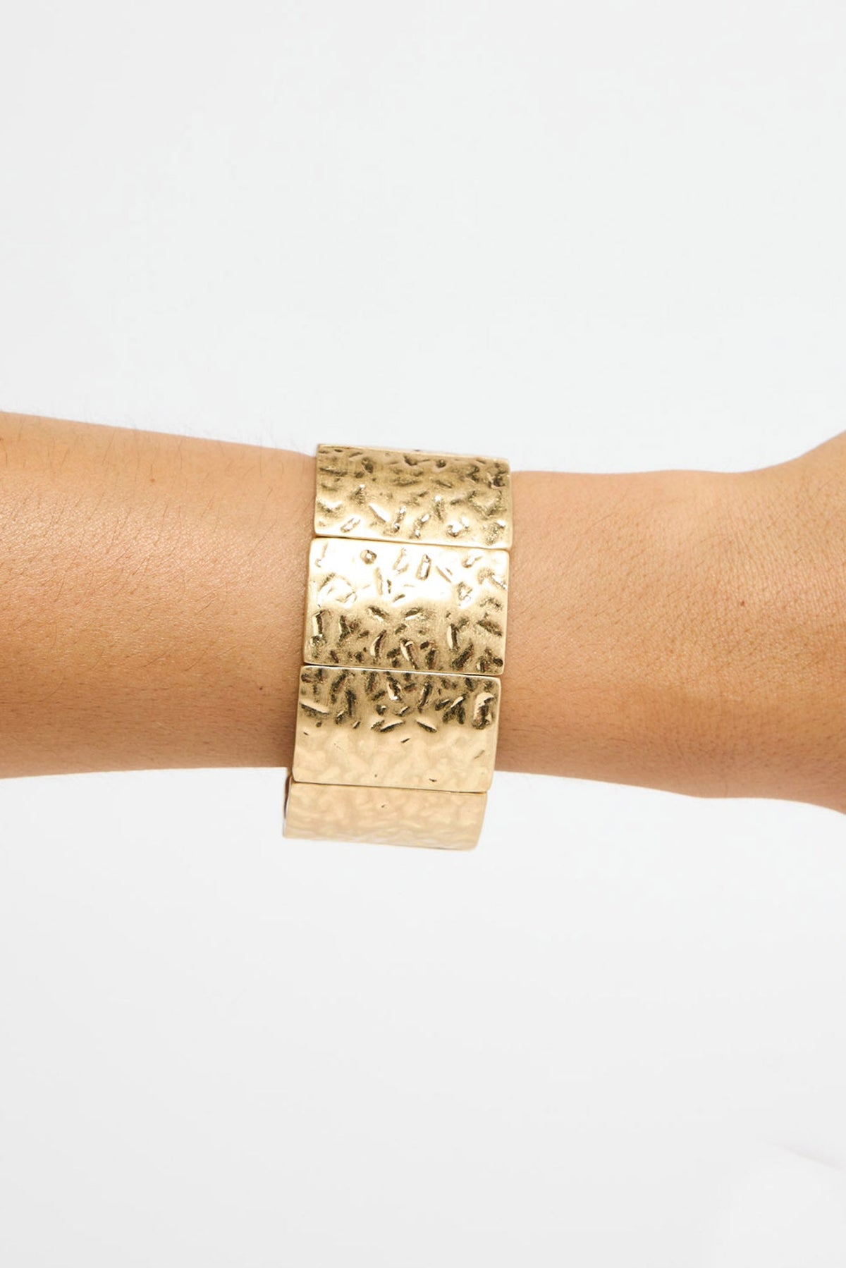 Close-up of a model wearing the wide gold-tone hammered cuff bracelet on their wrist