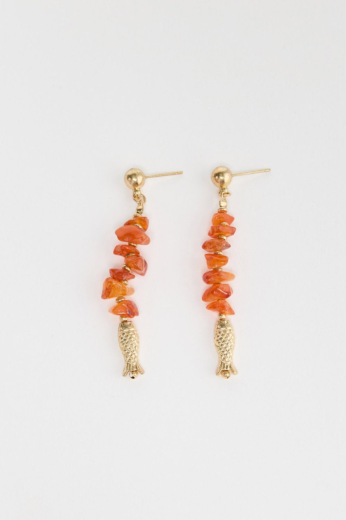 Pair of long drop earrings with a gold ball stud, a strand of orange carnelian stone chips and a small detailed gold-tone fish charm at the base, laid flat on a white background