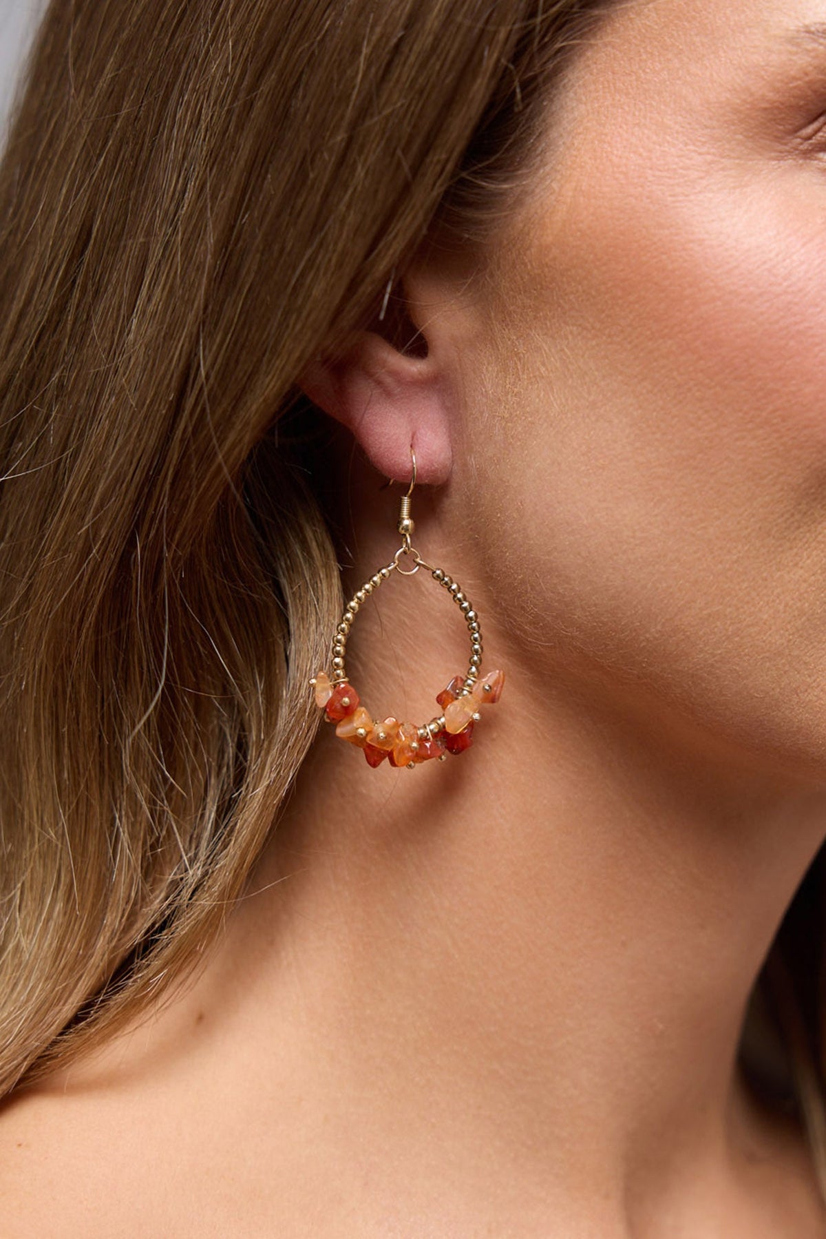 Close-up of the Yalla hoop earring worn on the ear, showing the gold beaded hoop and orange stone chip cluster against the hair