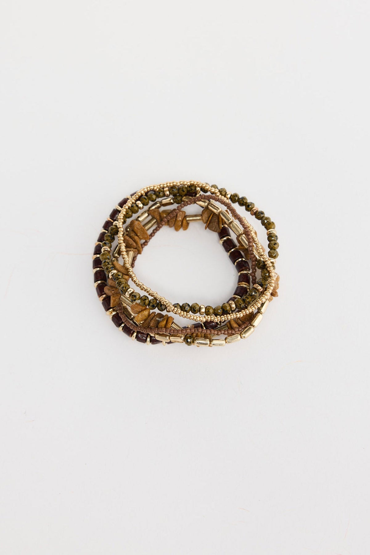Set of six stretch bracelets in earthy natural tones including dark wood rounds, olive green crystals, tiger eye stone chips, gold-tone tubes and brown seed beads, shown coiled together on a white background