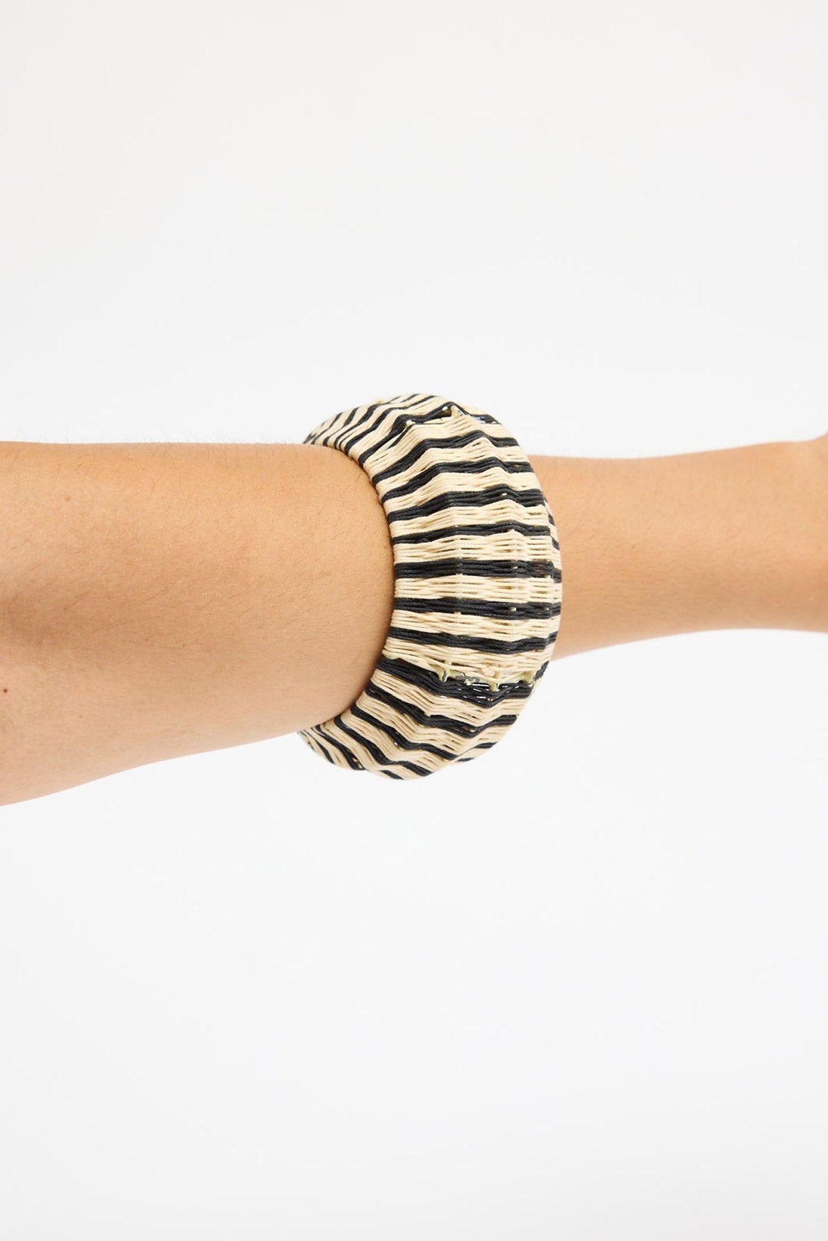 Chunky round bangle woven in natural cream and black raffia in a bold vertical stripe pattern, shown at an angle on a white background