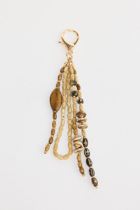 Multi-strand keyring charm with three dangling strands of natural cream and brown oval wood beads, a large tiger eye oval bead, carved dark wood discs with cross motifs and gold-tone accent beads, attached to a gold-tone lobster clasp on a white background