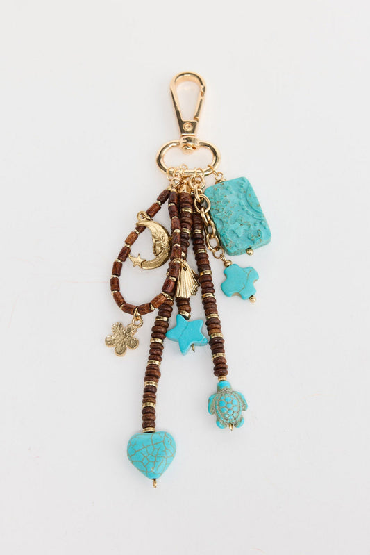 Cluster keyring charm with multiple strands of brown wood disc beads and turquoise stone charms including a heart, star, cross and rectangular pendant, plus a gold-tone sea turtle charm, crescent moon and mini tassel, attached to a gold-tone swivel clip on a white background