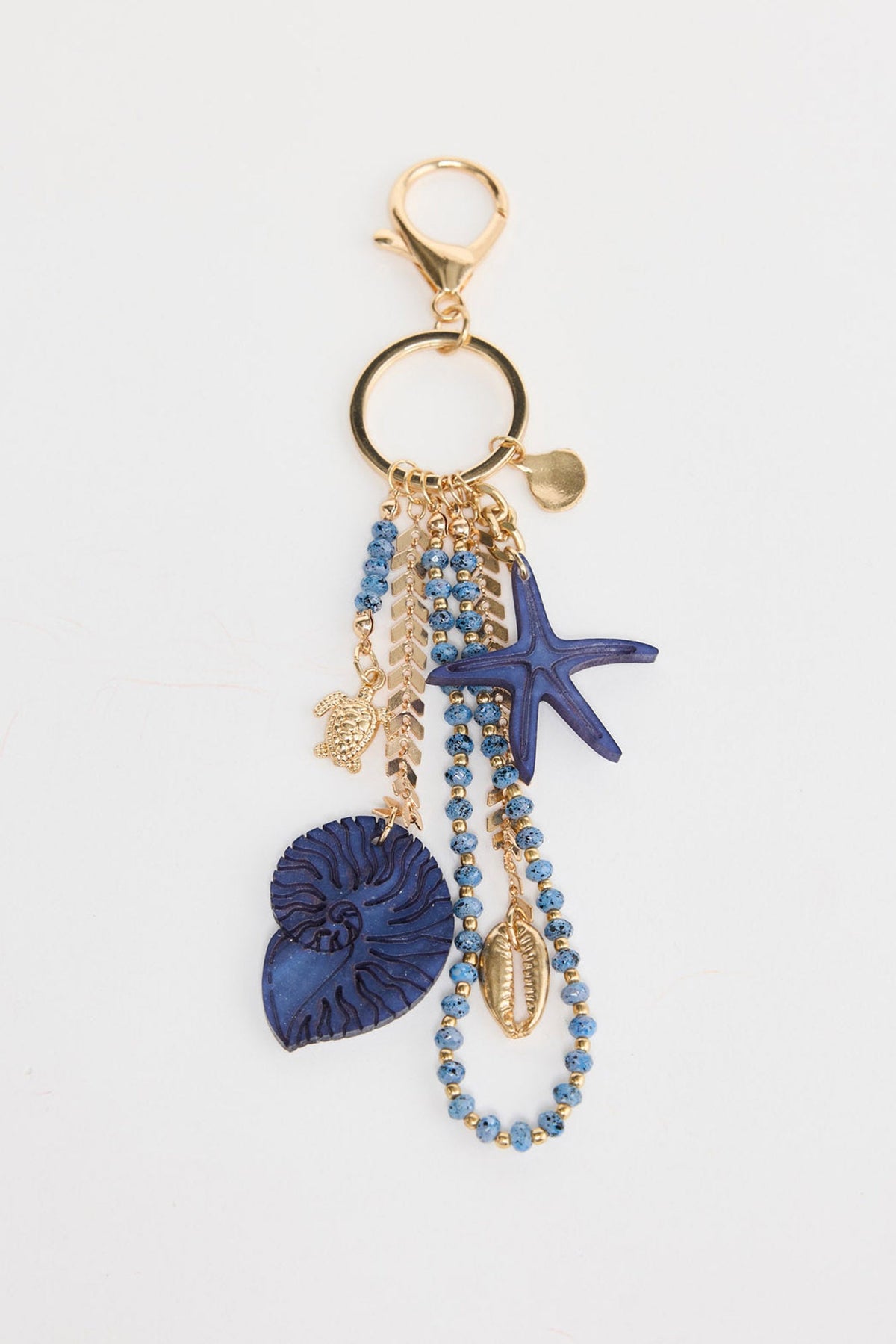 Cluster keyring charm with strands of blue speckled crystal beads and gold-tone chain, featuring a large navy blue resin starfish, a carved navy nautilus shell pendant, a gold-tone cowrie shell charm and a small gold sea turtle charm, attached to a gold-tone lobster clasp and split ring on a white background