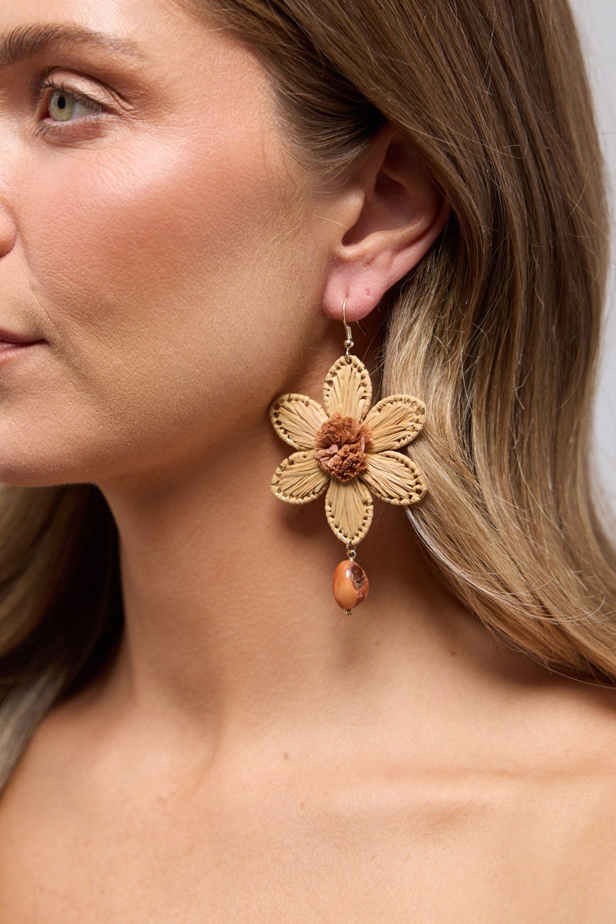 Tribal Flower earring in Natural worn on the ear, showing the raffia petal detail and dangling stone bead up close