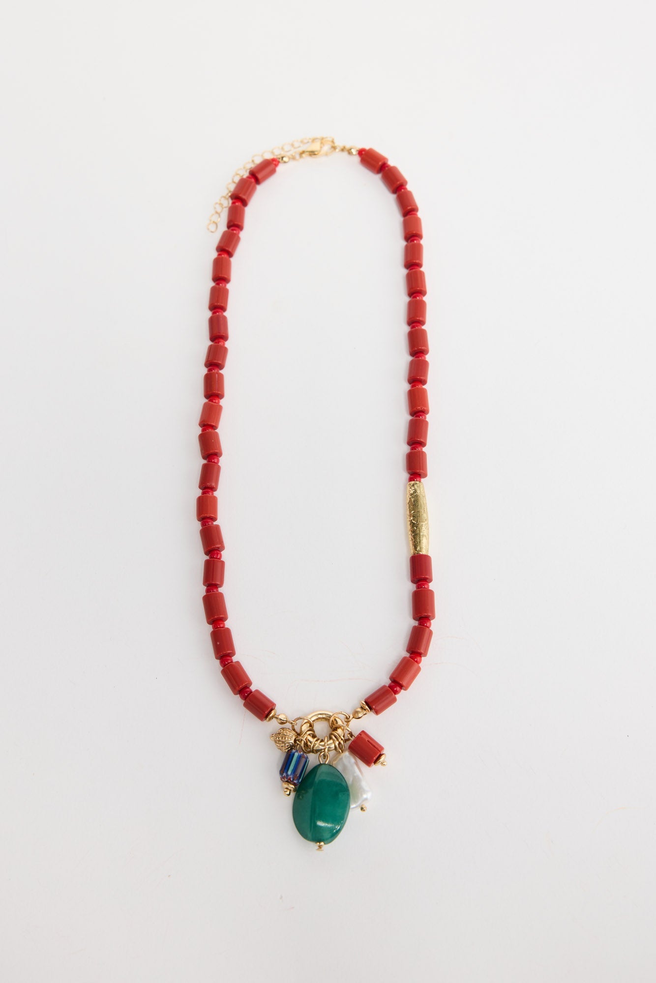 Elias beaded necklace laid flat, showing the red bead strand with a gold accent tube and a charm cluster of green stone, pearl and multicolour beads