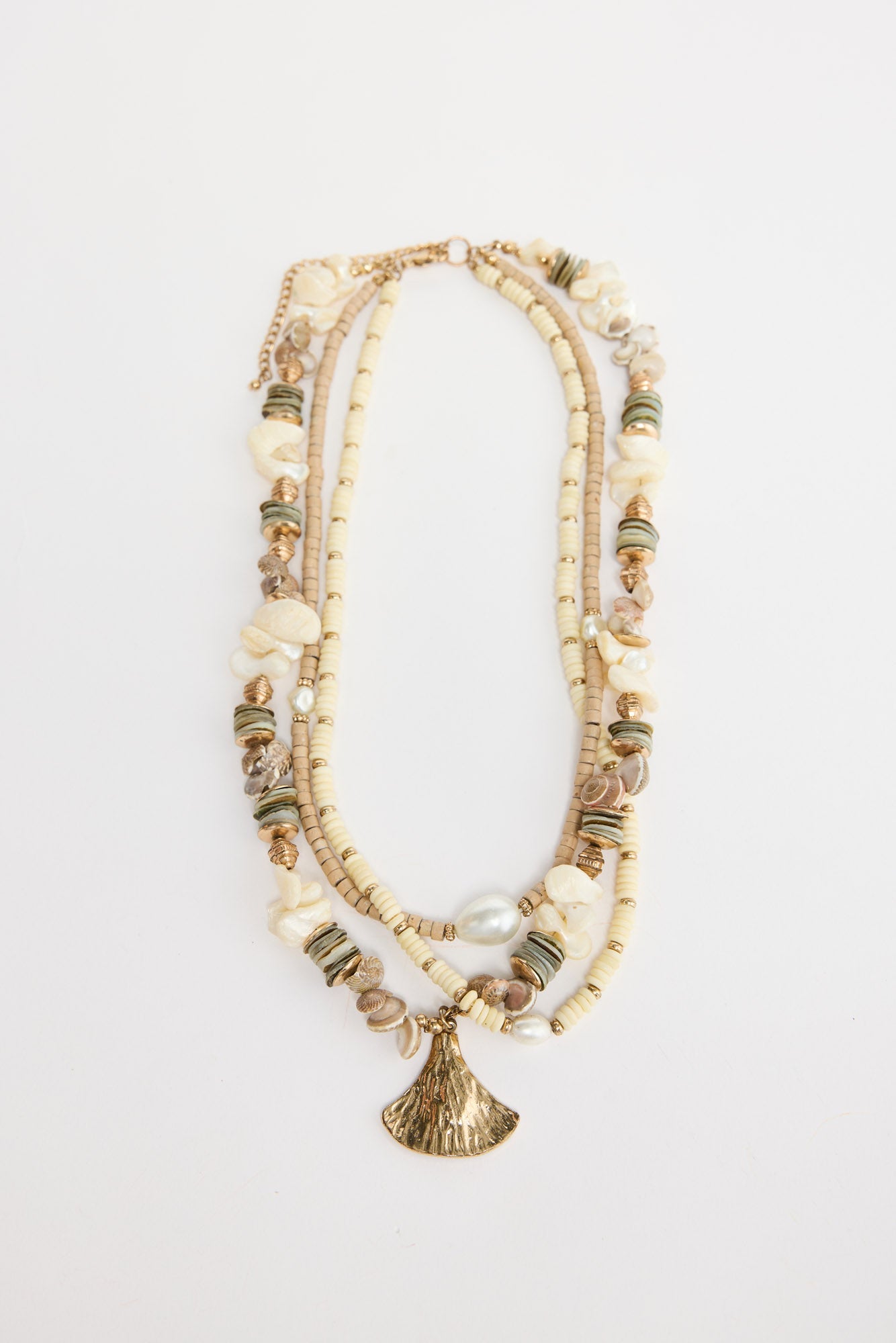 Otis multi-strand necklace laid flat, showing cream and tan disc beads, shell chip accents, pearls and a gold-tone fan pendant