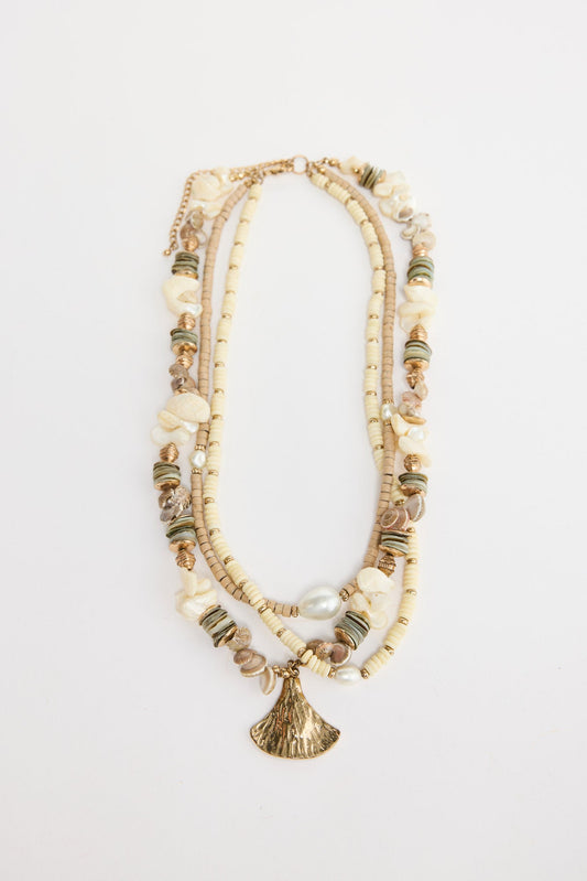 Otis multi-strand necklace laid flat, showing cream and tan disc beads, shell chip accents, pearls and a gold-tone fan pendant
