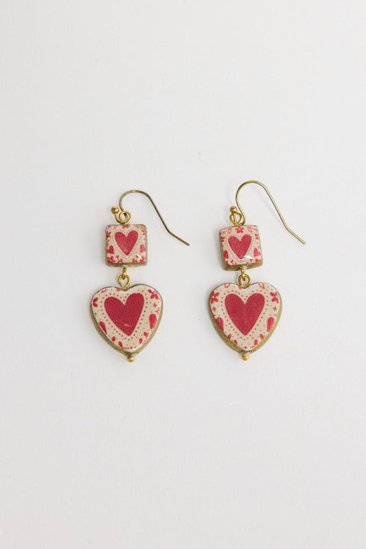 Pair of Love Sick drop earrings in Red laid flat, showing the square heart-print charm and heart-shaped drop