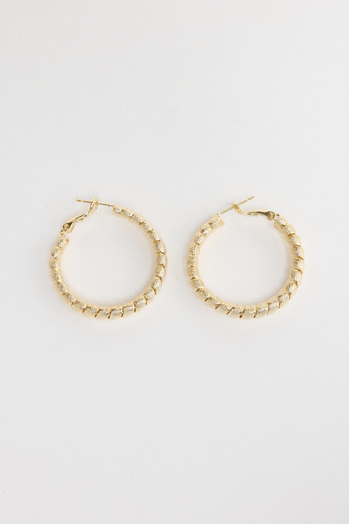 Neela Earrings in Gold – twisted, textured gold-tone hoop earrings shown flat on a white background.
